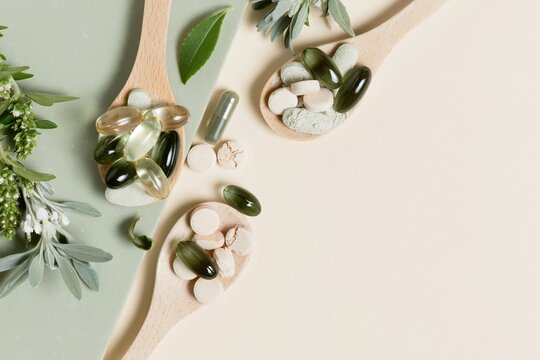 Wooden spoons filled with green fish oil softgels and herbal tablets on a sage stone surface for a natural wellness and nutrition concept with copy space