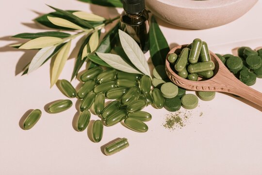 Green herbal supplement capsules and tablets scattered on a light surface with a wooden spoon and dropper bottle for natural wellness marketing