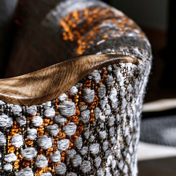 Woven upholstery fabric with geometric pattern and a waxed oak wood armrest, featuring tactile slub yarn and warm side lighting for textile design libraries