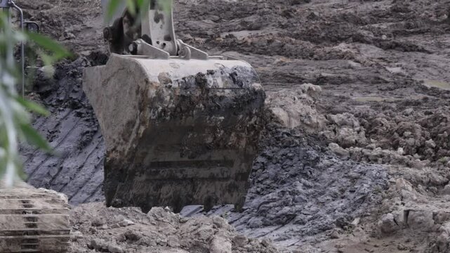 Raw industrial energy and relentless earth-moving force dominate the scene; dark, clumped soil and rugged machinery convey heavy labor and extraction