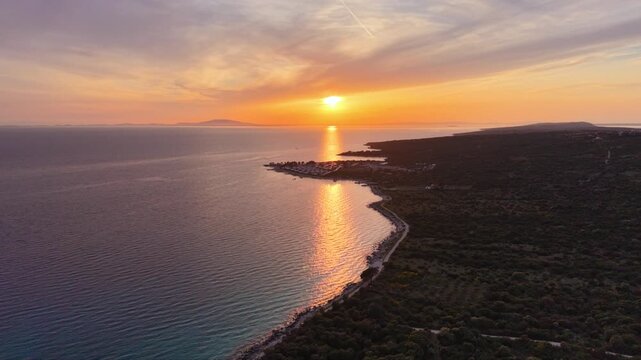 Aerial sunset view of a modern seaside holiday resort on Pag Island, Croatia, with rows of contemporary villas, private pools, landscaped paths and a small beach beside the calm Adriatic Sea.