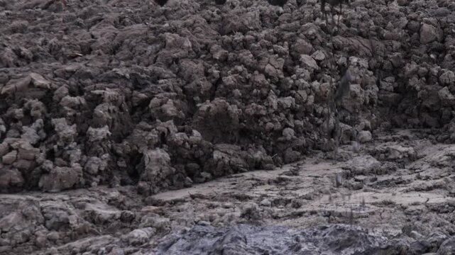 Raw industrial energy and relentless earth-moving force dominate the scene; dark, clumped soil and rugged machinery convey heavy labor and extraction