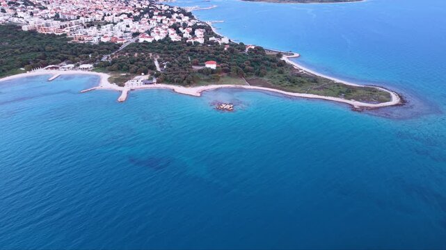Aerial panoramic view of Novalja, Croatia, showing the coastal town&rsquo;s dense red-roofed architecture, lively central promenade and traditional churches, with the dramatic rocky mountains of Pag Island 