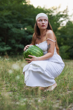 Young woman crouching on green grass and holding large watermelon