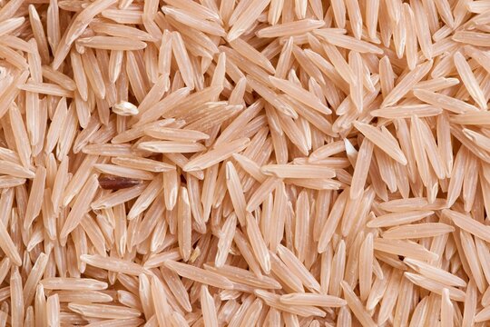 Slender long grain dry rice kernels in a dense heap provide a warm organic texture background for food packaging and healthy carbohydrate concepts