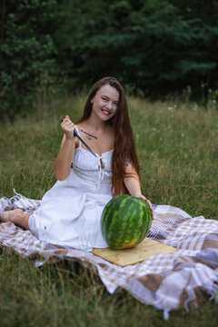 Smiling young woman holding knife to cut large watermelon on picnic blanket
