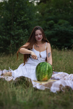 Young woman looking down while cutting watermelon on picnic blanket