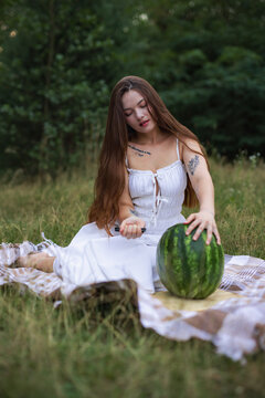 Young woman looking down while cutting watermelon on picnic blanket