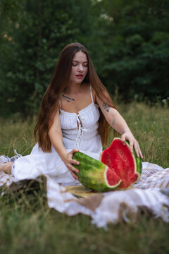 Young woman opening two halves of fresh cut watermelon on picnic blanket