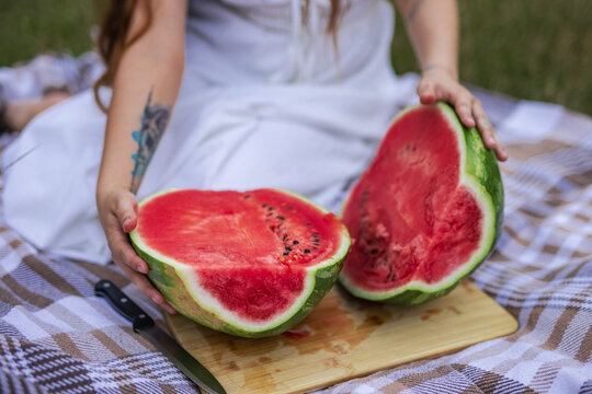 Close up of young woman holding two halves of ripe red watermelon on picnic