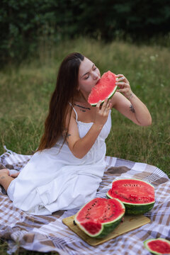 Young woman sitting on picnic blanket and eating slice of ripe watermelon