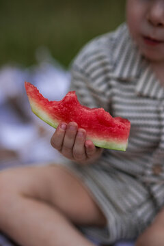 Close up of toddler boy hand holding bitten slice of fresh red watermelon