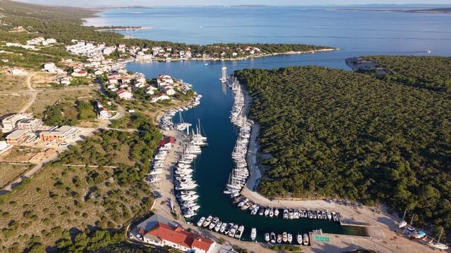 High aerial view of Luka &Scaron;imuni marina on Pag Island, Croatia, with rows of yachts and sailboats moored in a narrow sheltered harbor beside a coastal village and forested peninsula on the Adriatic Sea
