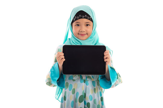 Adorable Muslim girl in mint green hijab showing empty tablet screen mockup smiling at camera in white studio.