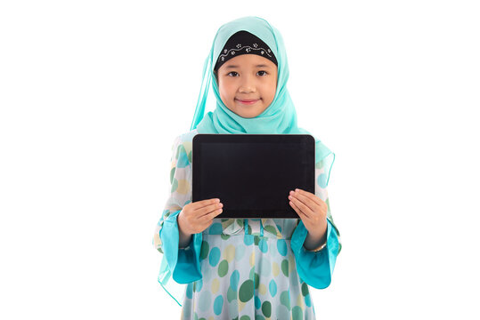 Adorable Muslim girl in mint green hijab showing empty tablet screen mockup smiling at camera in white studio.