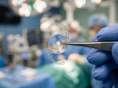 Gloved Hand Holding Artificial Intraocular Lens With Tweezers