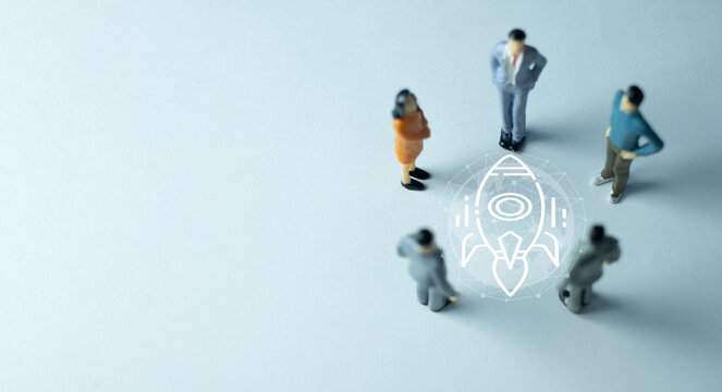 Business startup and global project launch concept. Miniature business people surrounding a digital rocket ship and wireframe globe graphic on a light blue background with copy space.