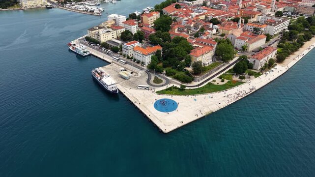 High aerial view of Zadar Old Town in Croatia, showing the historic peninsula with dense red-tiled roofs, church towers, waterfront promenades, marina and the Adriatic Sea surrounding the city center.