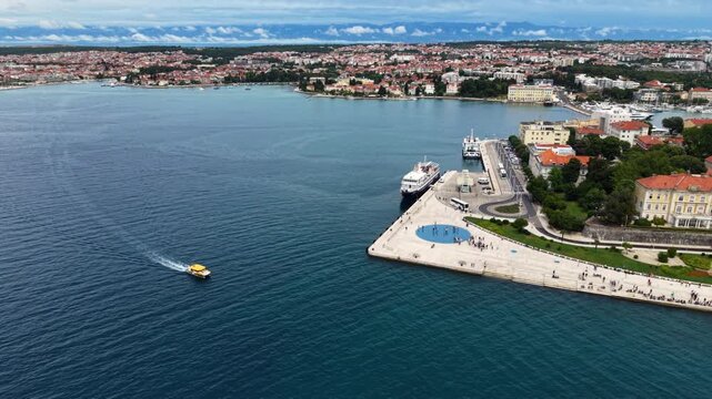 Wide aerial view of Zadar, Croatia, showing the historic old town peninsula, marina, waterfront and expansive Adriatic Sea, with a small passenger boat crossing the bay.