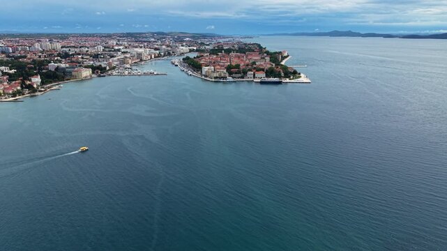 Wide aerial view of Zadar, Croatia, showing the historic old town peninsula, marina, waterfront and expansive Adriatic Sea, with a small passenger boat crossing the bay.