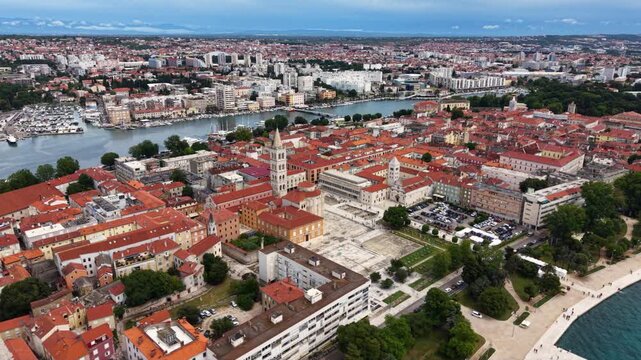Aerial view of the historic center of Zadar, Croatia, showing red tiled rooftops, church towers, Roman Forum ruins, waterfront promenade, marina and the surrounding modern city beside the Adriatic Sea