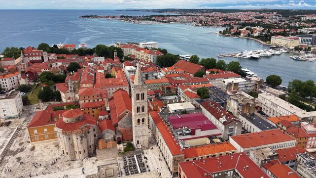 Aerial view of the historic center of Zadar, Croatia, showing red tiled rooftops, church towers, Roman Forum ruins, waterfront promenade, marina and the surrounding modern city beside the Adriatic Sea