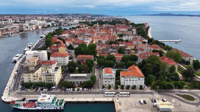 Aerial view of the historic center of Zadar, Croatia, showing red tiled rooftops, church towers, Roman Forum ruins, waterfront promenade, marina and the surrounding modern city beside the Adriatic Sea