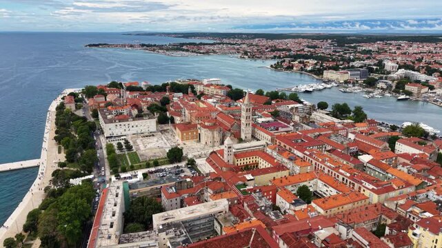 Aerial view of the historic center of Zadar, Croatia, showing red tiled rooftops, church towers, Roman Forum ruins, waterfront promenade, marina and the surrounding modern city beside the Adriatic Sea