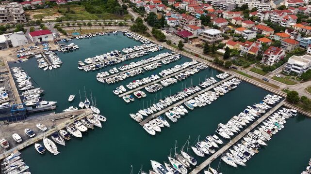 Aerial view of a densely packed coastal marina with hundreds of motorboats, yachts and sailboats moored along parallel floating docks beside the Adriatic Sea.