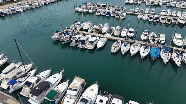 High aerial view of Luka Sukosan marina on the Croatian Adriatic coast, with long breakwaters, rows of moored yachts and sailboats, a coastal town and forested hills extending along the shoreline. 