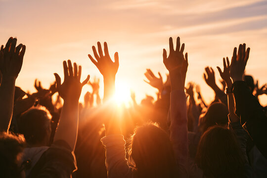 With palms facing upwards, a crowd raises their hands towards the sunset