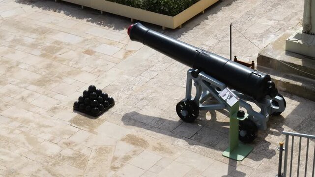 single saluting cannon beside a stacked cannonball pile coat of arms pedestal upper barrakka artillery display saluting battery cannon valletta artillery historic cannon detail malta gun battery
