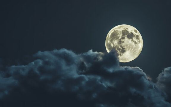 Full Moon Glowing Behind Dark Clouds in Night Sky