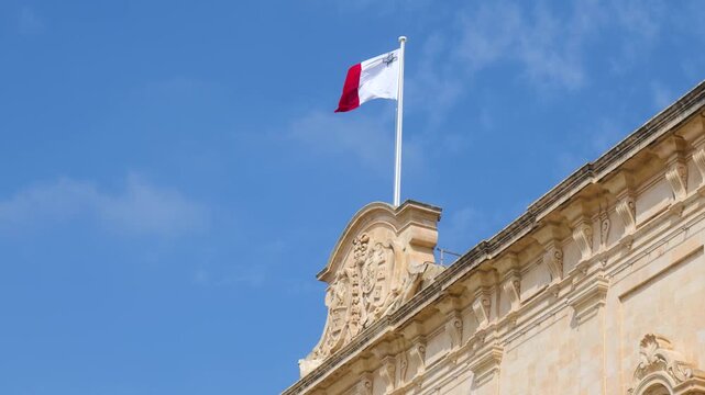 maltese flag waves atop the auberge de castille pediment close up view of the ornate baroque roofline malta national flag flag close up valletta baroque palace malta symbol flag pole malta
