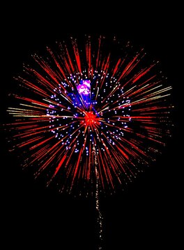 Vibrant red and purple fireworks exploding in the dark night sky. Bright radial light rays and smoke trails against a black background. Perfect for celebration and festive event concepts.
