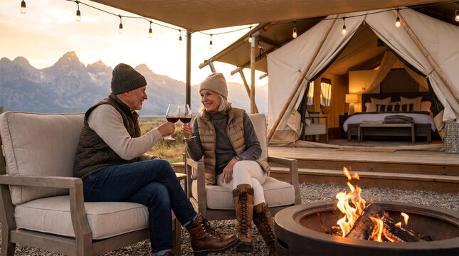 Glamping 003 Senior Couple Toasting with Wine Glasses on Outdoor Sofa near Campfire at Luxury Glamping Tent During Sunset（夕暮れ時の豪華なグランピングテント前で焚き火を囲みソファーに座ってワインで乾杯するシニア夫婦）