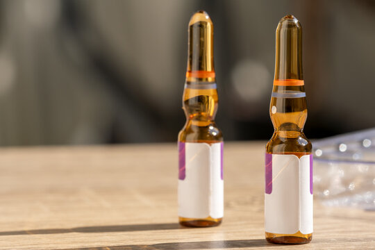 Two amber glass pharmaceutical ampoules with blank labels on a wooden surface. Represents injectable medication, clinical treatment and pharmaceutical healthcare products.