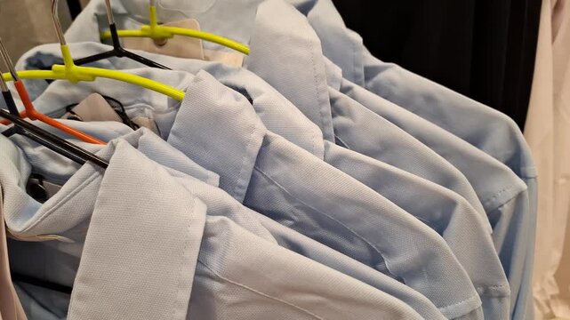 Light blue shirts hanging on hangers inside a clothing store. clothing retail, office apparel, fashion store.