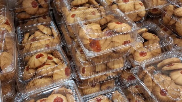 Cookies with red jam filling inside clear plastic containers on a store shelf. confectionery dessert, sweet treat, retail packaging.