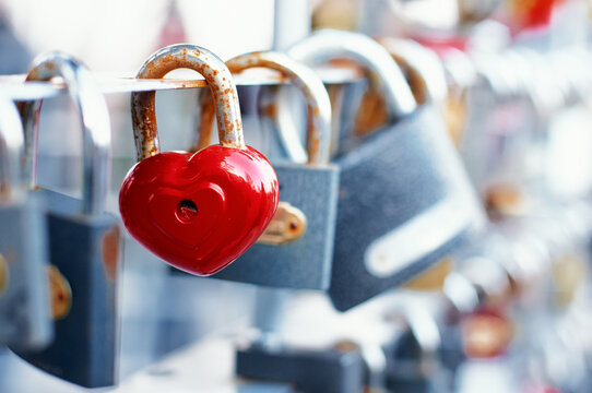A closeup of a red, heart-shaped padlock affixed to a bridge railing among other locks, symbolizing love, unity, and enduring affection, commonly associated with romantic