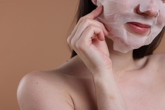 Woman with sheet face mask on beige background, closeup