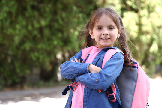 Happy little girl with backpack outdoors, space for text