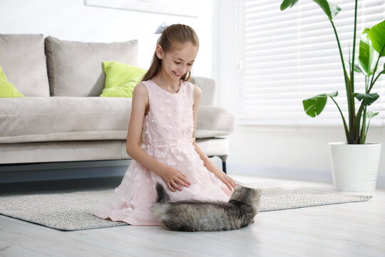 Smiling little girl in dress with her cute cat on floor at home