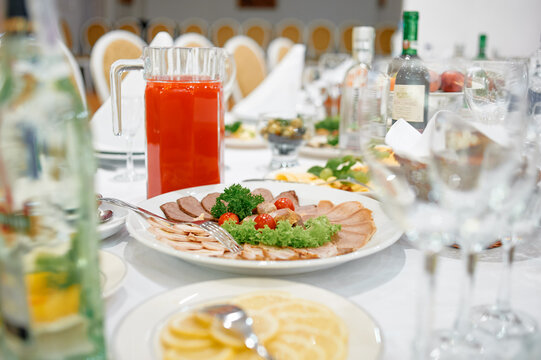 banquet table set for wedding reception featuring platters of cold cuts, fresh lettuce and cherry tomatoes, pitchers of juice, bottles and glassware conveying a festive, catered dinner atmosphere