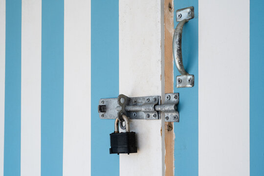 Weathered padlock, metal latch and handle on blue and white striped wooden door