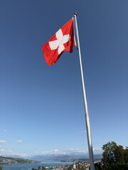 Fototapeta premium Waving Swiss Flag with Lake and Alps in the Background, Switzerland