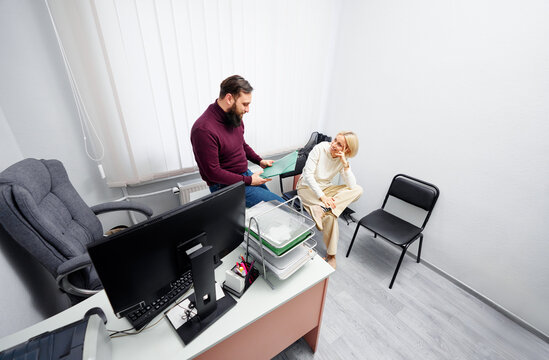 Two professionals in a compact office review documents as a computer and organized trays sit on a desk, showing collaboration, focus, and a calm, productive workplace environment.