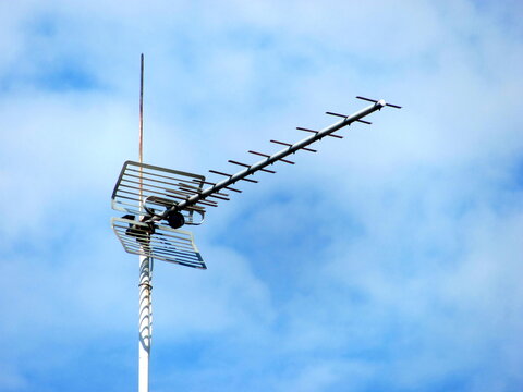 A metal UHF television antenna mounted outdoors against a partly cloudy blue sky
