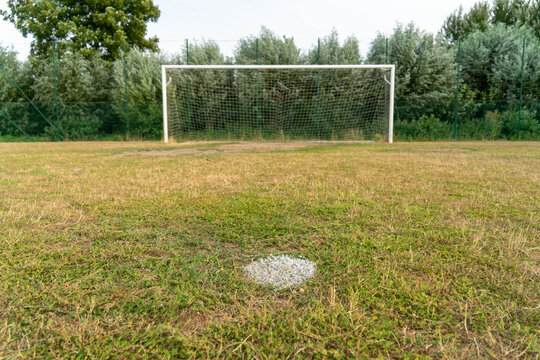 Close-up of a penalty spot mark on dry grass with a soccer goal out of focus in the background