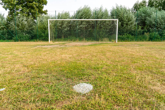 Close-up of a penalty spot mark on dry grass with a soccer goal out of focus in the background
